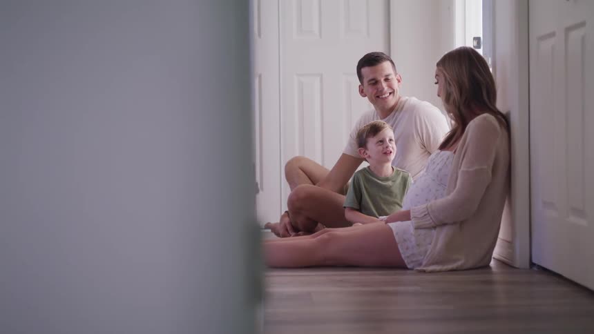 A man a woman and a boy sitting on the floor of a hallway with a door in the background