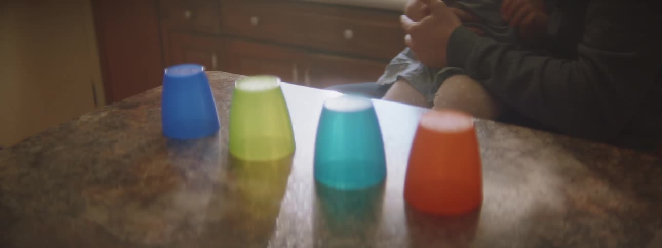 Baby sitting on parent's lap wants to play with colorful plastic cups over the kitchen table
