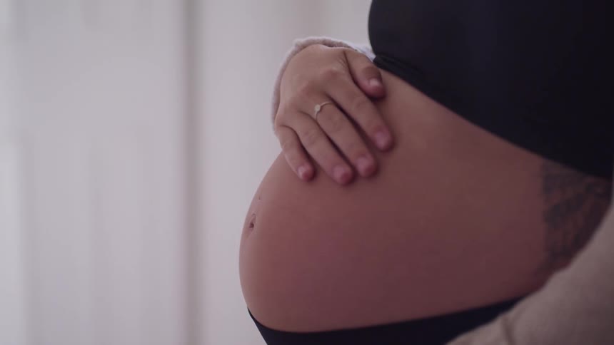 A pregnant woman is touching her stomach indoors