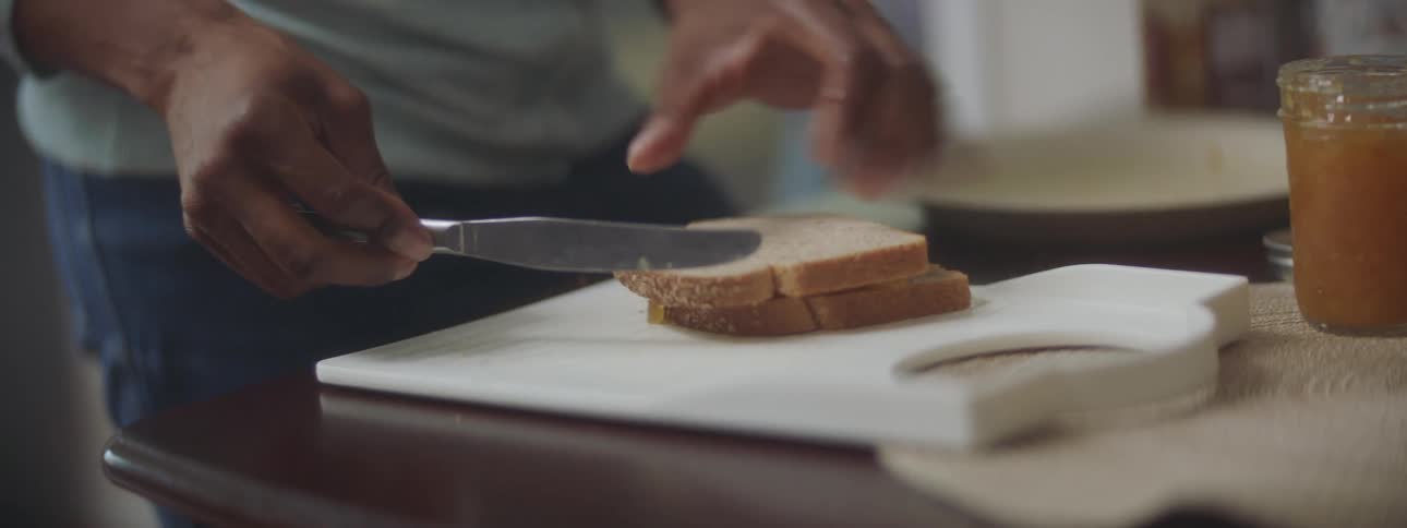 A person in a kitchen standing by a table making a peanut butter and jelly sandwich