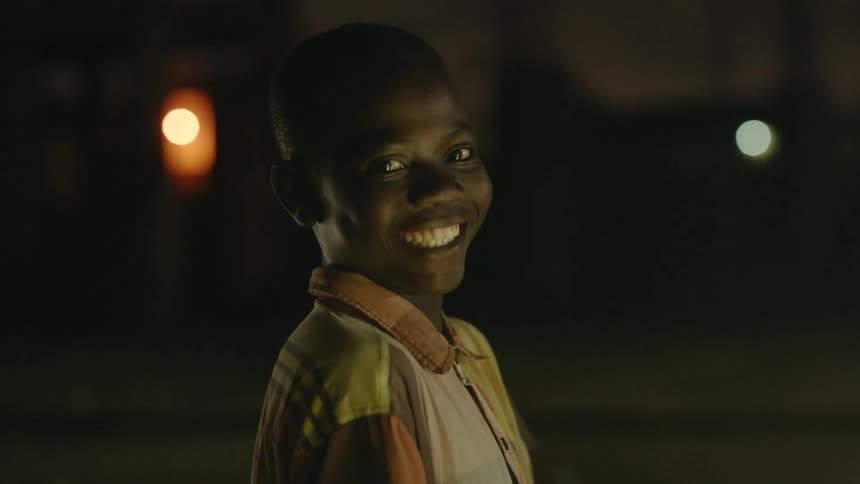 Young boy smiles and aughs looking at the camera on a street at night