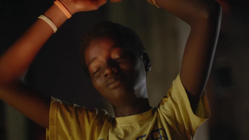 Young teenage girl slowly dancing with her arms over her head inside a dimly lit room