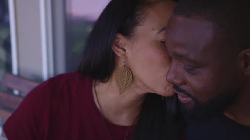 Woman kisses her husband in the cheek sitting in a bench outdoors