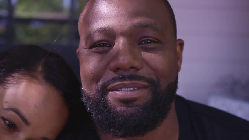 A man smiling and staring as a woman lays her head on his shoulders