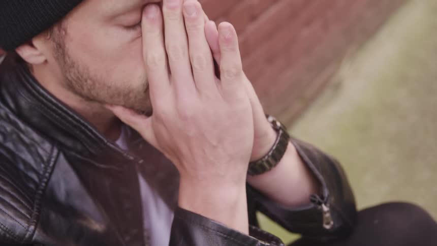 A man is sitting outdoors by a wall