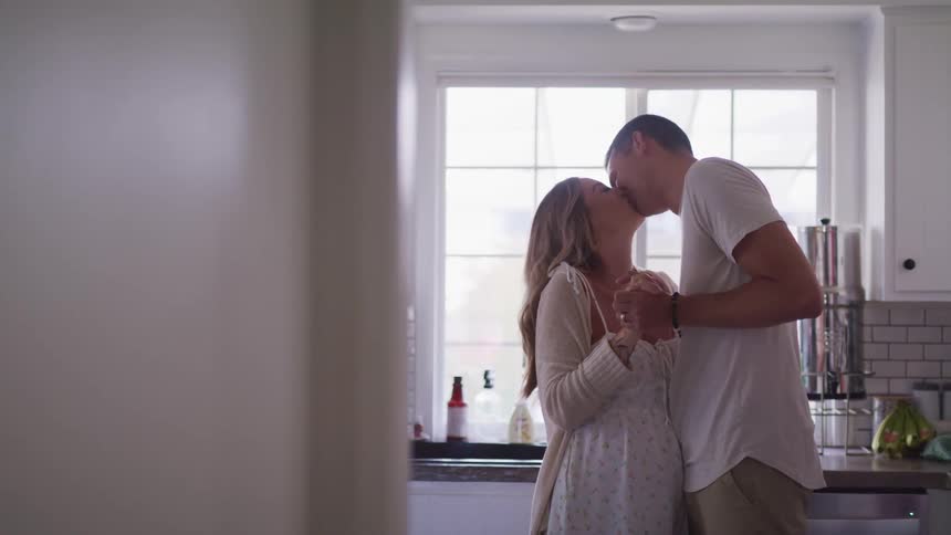 Young pregnant couple kissing and hugging lovingly in the kitchen at home