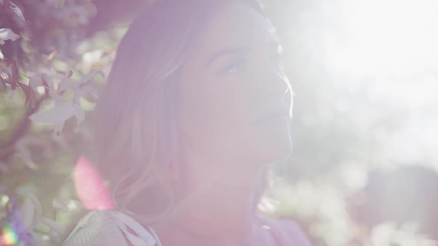 A woman standing with makeup next to a tree with the sky and clouds in the background