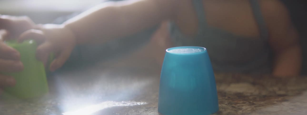 A parent uses colorful plastic cups to play with their toddler over a table at home
