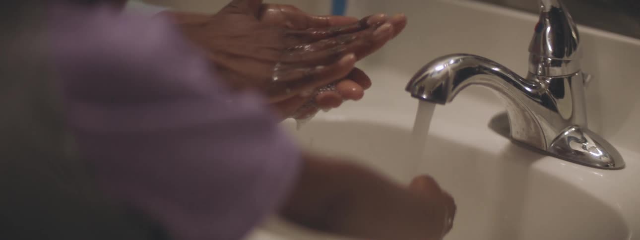 A person washing a childs hands in a sink with a mirror in the background