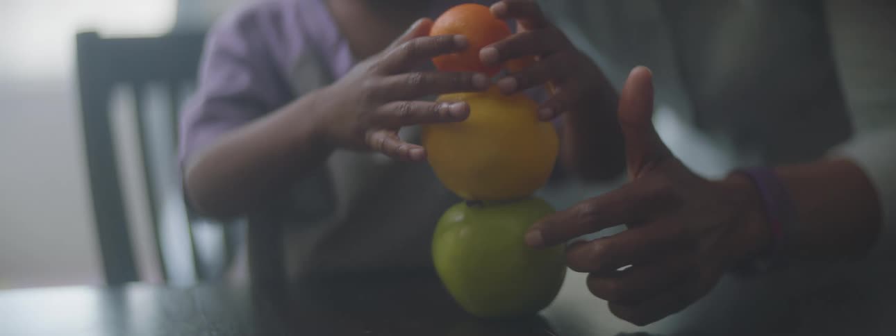 A child stacking fruit on a table with their parent