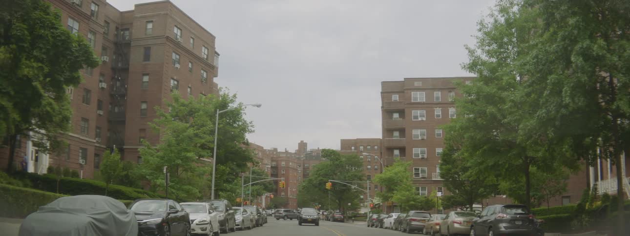 Cars traveling on a city street near brick buildings and trees