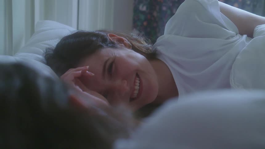 A man and a woman in love in a bedroom laying in bed smiling