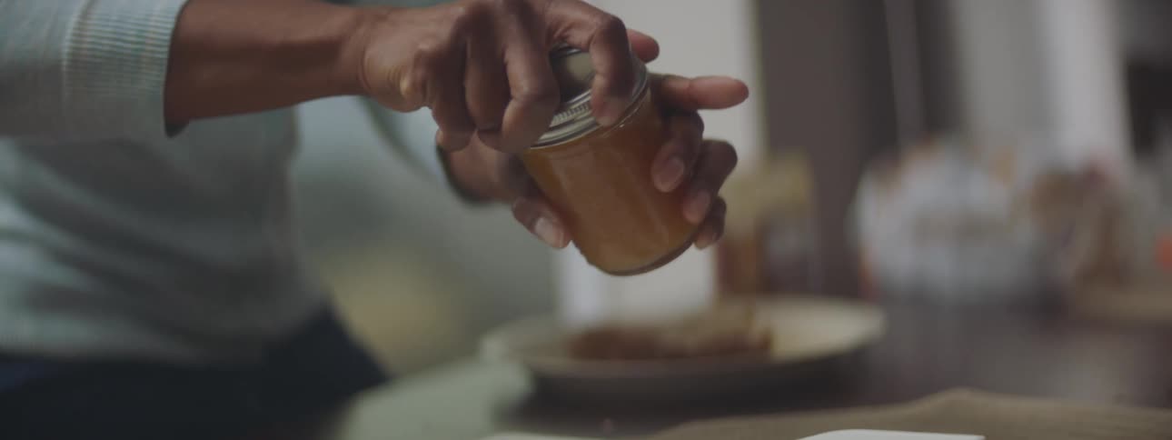 Mother in a kitchen closes jar while making a peanut butter and jelly sandwich