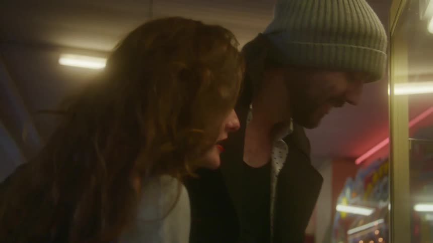 A man and a woman in an arcade laugh as they look at a game on a date