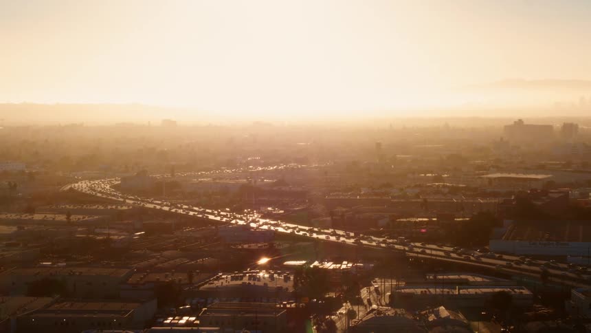 Busy city highway with many cars as a bright sun shines in an orange sky