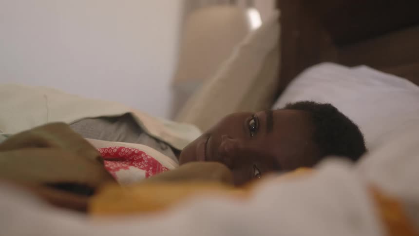 A boy in a bedroom laying in a bed with sheets and pillows