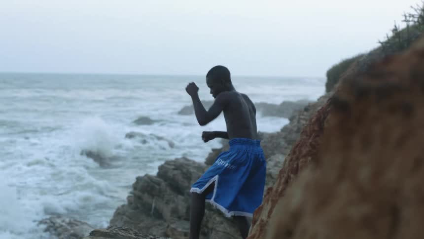 A shirtless boy punching the air while standing on a beach