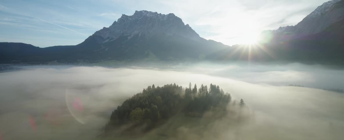 Sun shining brightly between mountains above the clouds