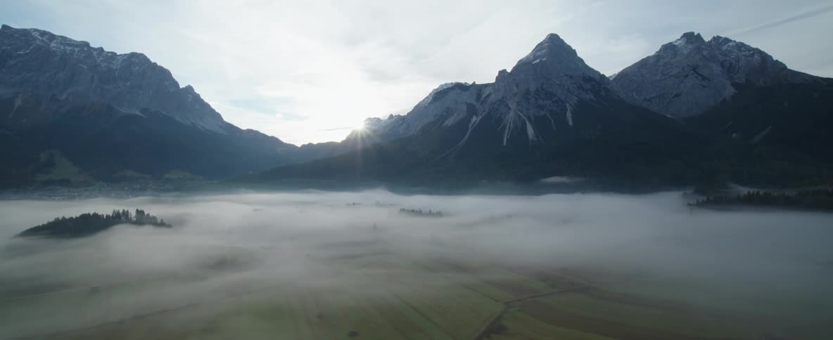 Sun shining between snow covered mountains above the clouds