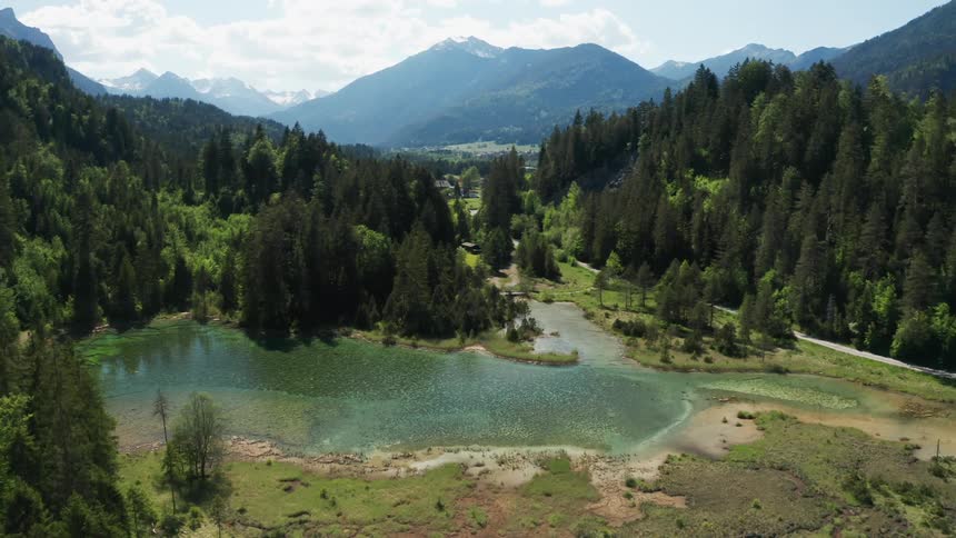 The surface of the water shimmers in the sunlight with forest and mountains around