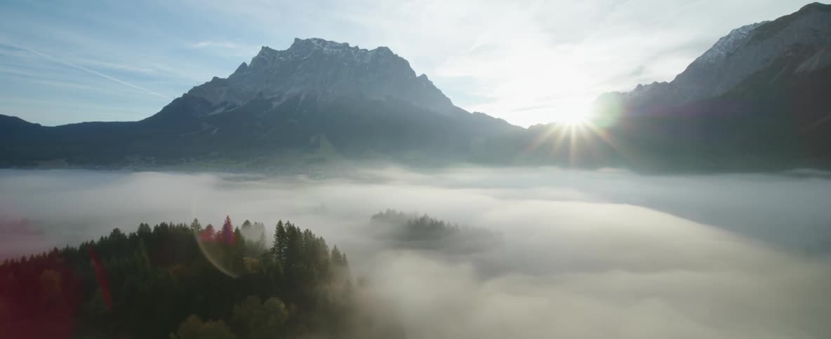 Sun shining brightly between mountains above the clouds