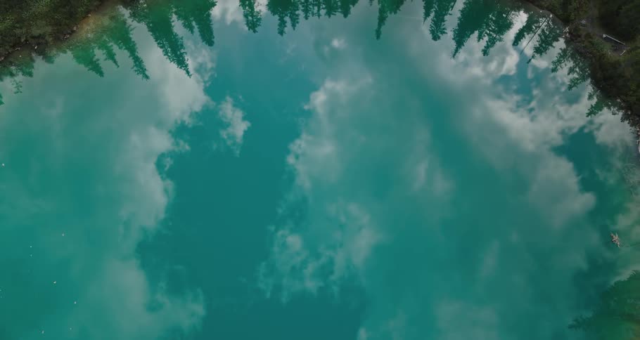 A pond surrounded by trees with the reflection of the sky and clouds reflecting off of it