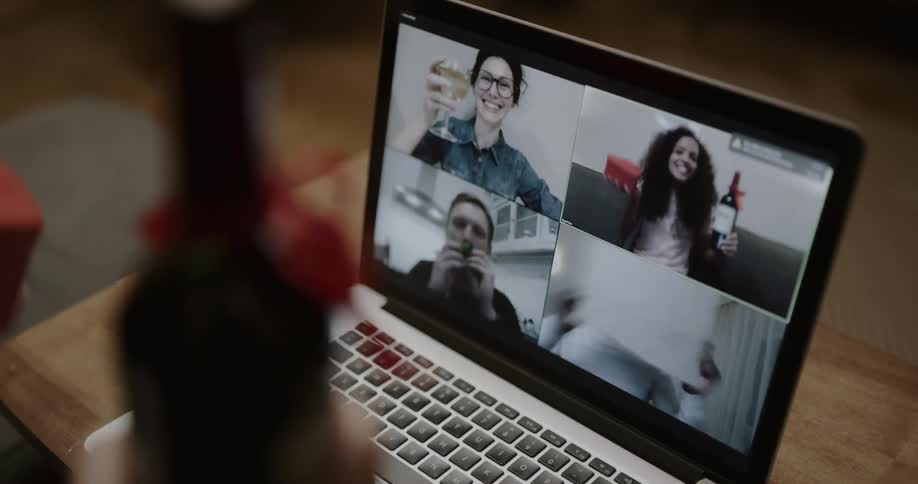 A woman in a room holding a bottle of wine and a box of chocolates while video chatting on a laptop