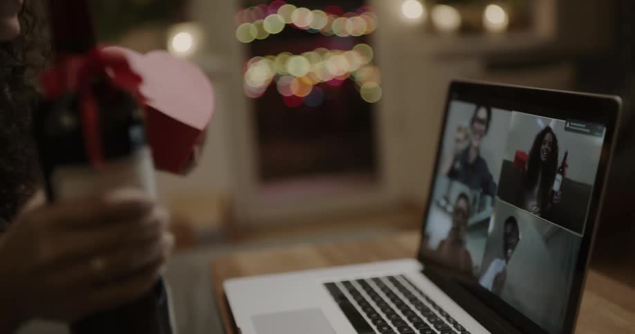 A woman in a room holding a bottle of wine and a box of chocolates while video chatting on a laptop