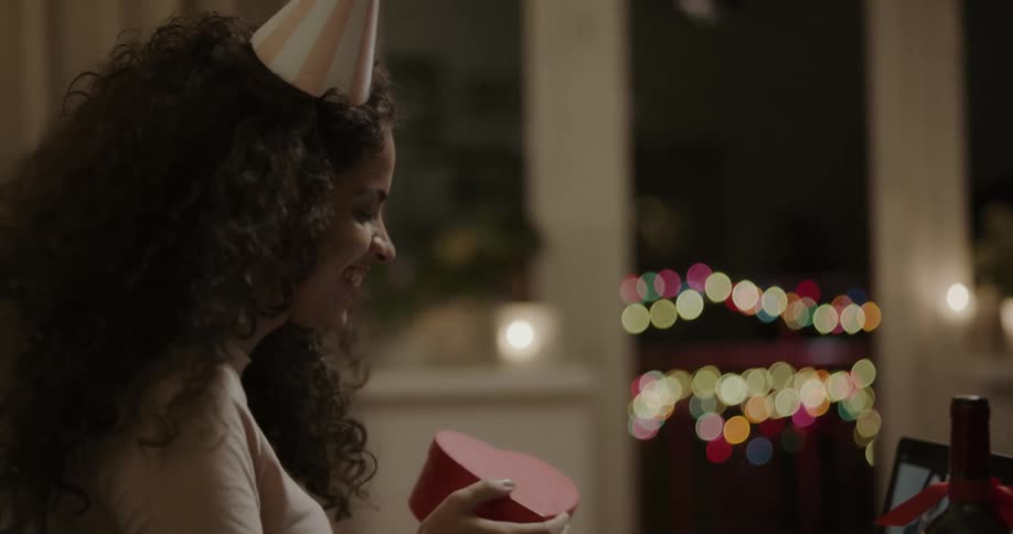A woman opens a gift box while in front of a laptop having a video call