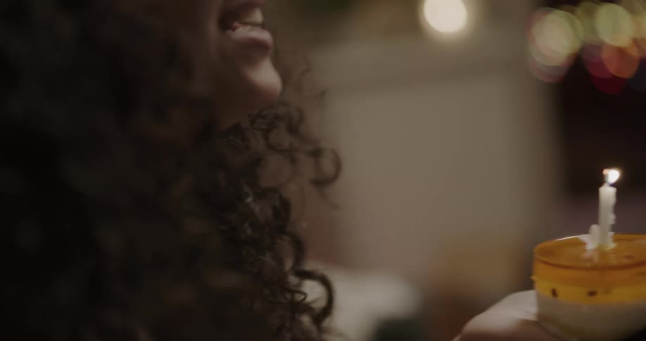 A woman video chats with friends on a laptop as she blows out a candle on a dessert and they hold up signs and drink wine