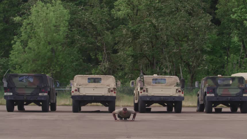 Man doing push ups in front of military jeeps