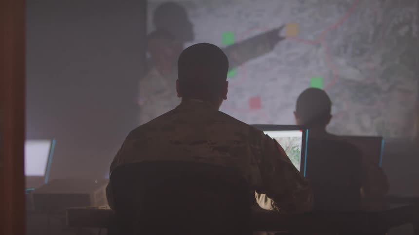 People in military uniforms in a room with laptops and a projection screen