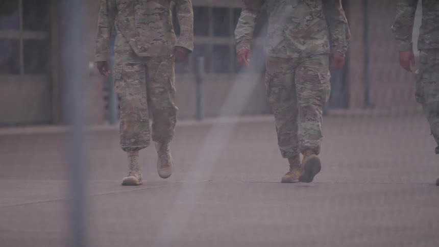 Three soldiers walk together behind the fence