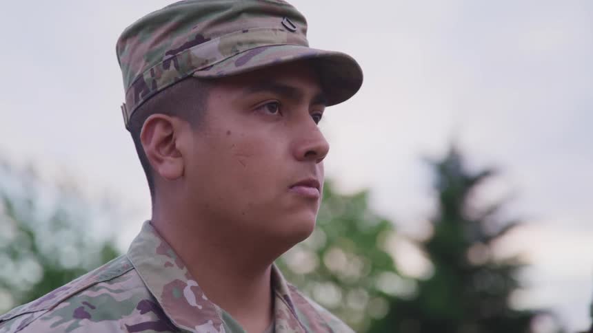 A soldier in camouflage saluting outside at sunset