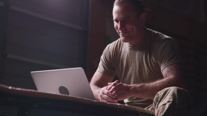 A soldier sitting and smiling at a laptop in front of him