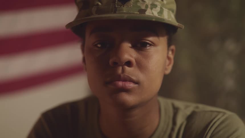 A woman with a military uniform staring in a room with an american flag in the background