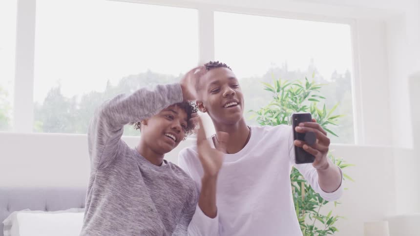 Teenage boys waving and smiling while face timing on cell phone