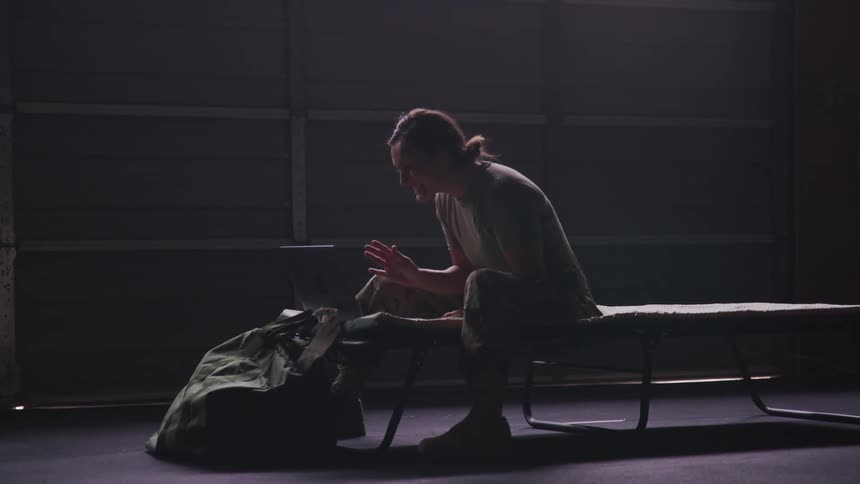 Military woman sitting on a bed waving in a video call through a laptop