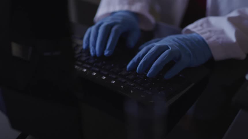 Person wearing blue gloves is typing on a keyboard