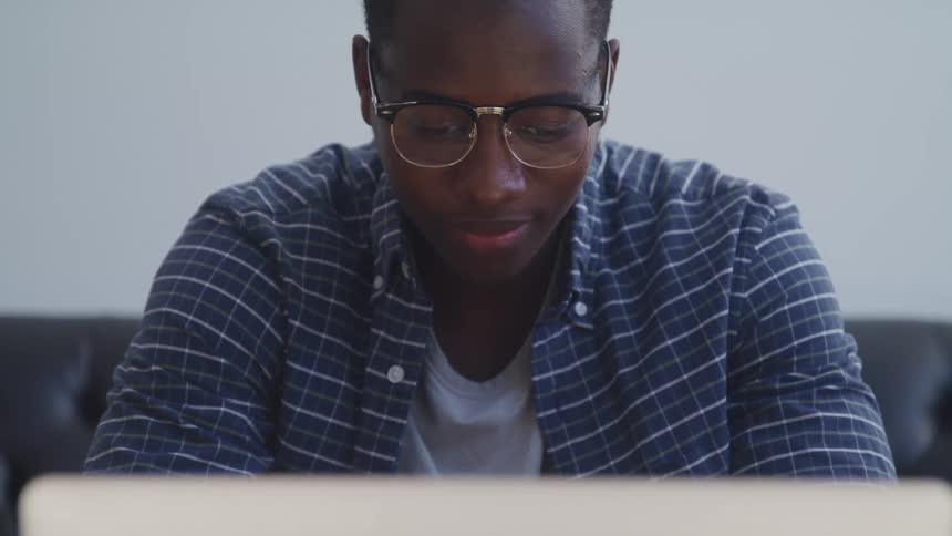 A teenage boy sits on a couch in front of a computer and concentrates