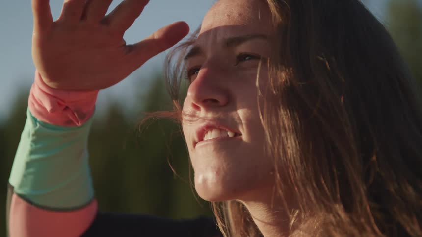 A woman shields the sun from her eyes with her hand while searching around in front of her