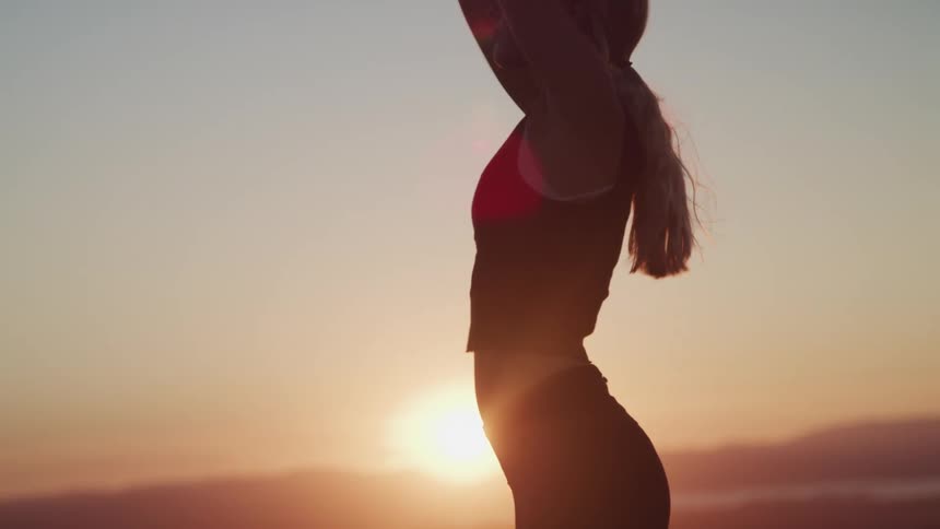 A woman stretching with a sunset a mountain range the sky and clouds in the background