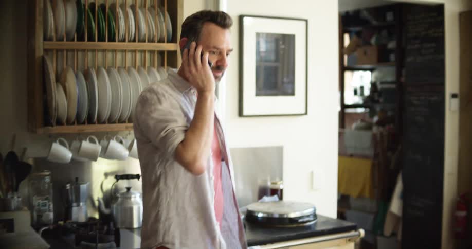 A man shakes his head as he talks on the phone in the kitchen
