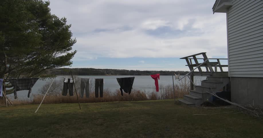 Clothes hang on a clothesline outside a home near a lake on a cloudy day