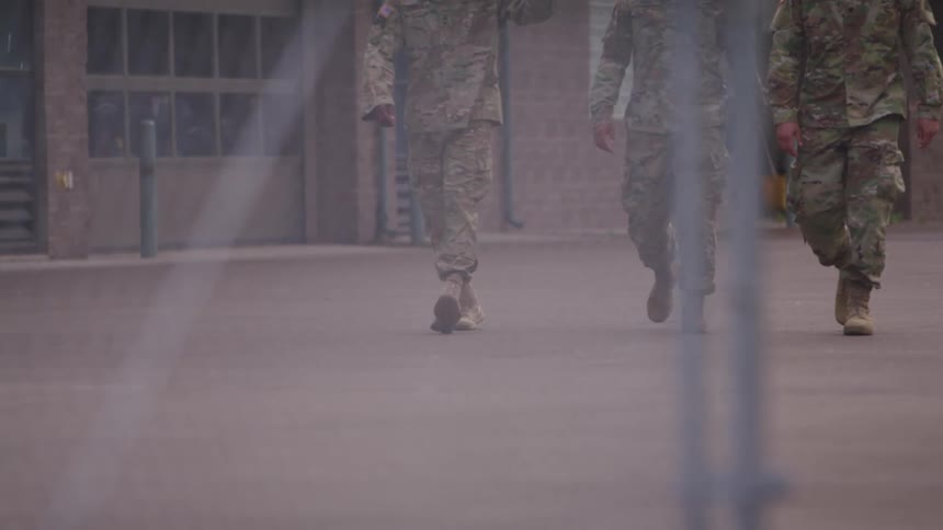 A group of american soldiers walking towards a wired fence in the yard near a building