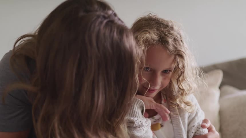 A mom hugs her daughter and smiles as they both wave at the laptop screen while sitting on the couch