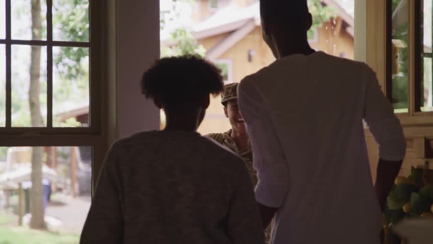 Two boys open a front door and hug a woman wearing a military uniform