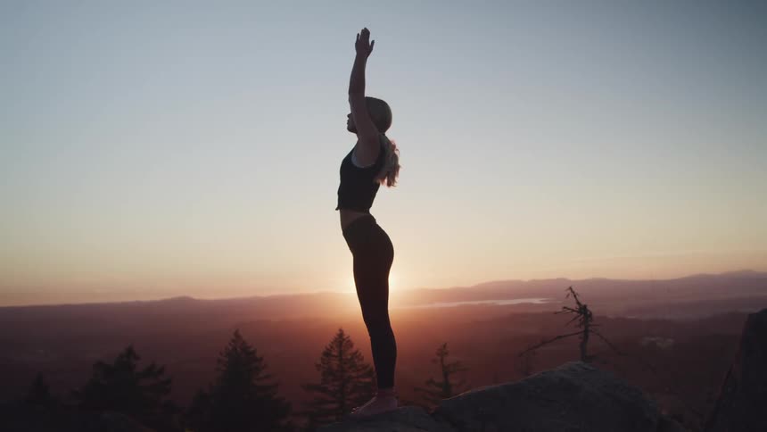 A silhouetted woman doing yoga outside at sunset