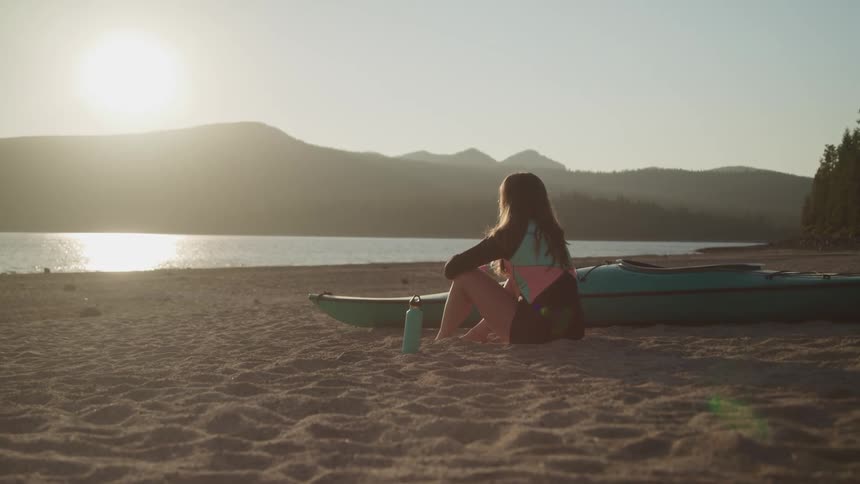 A woman is sitting on the beach at dusk