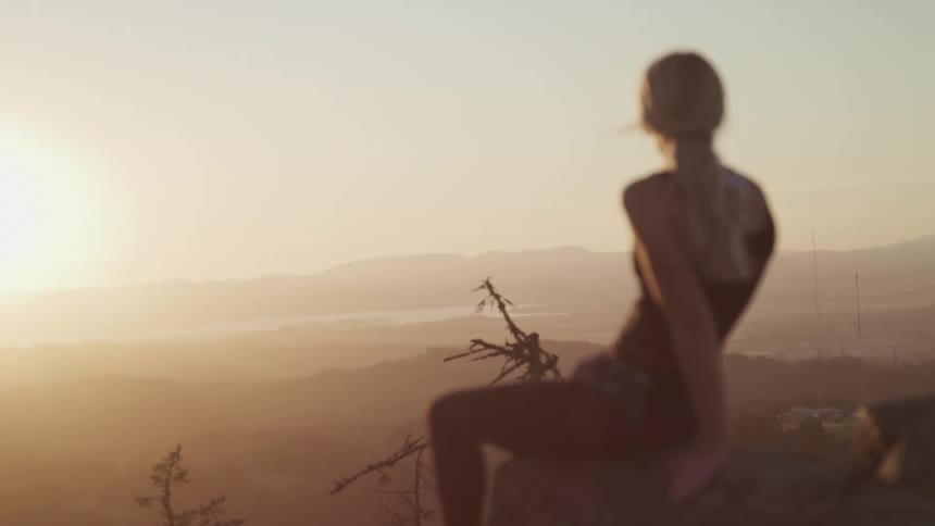 A woman sits on a cliff and looks out at the landscape
